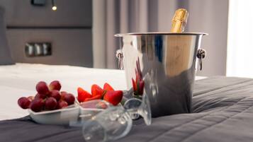 Um balde metálico com uma garrafa de champanhe, uma taça de uvas e um copo sobre uma cama.