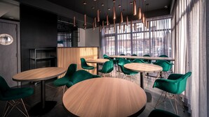 Een modern interieur met ronde tafels en groene stoelen, een houten scheidingswand en uitzicht door grote ramen.