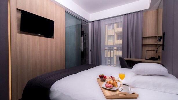 Hotelkamer met een bed, een wandtelevisie, een bureau en een raam met gordijnen.