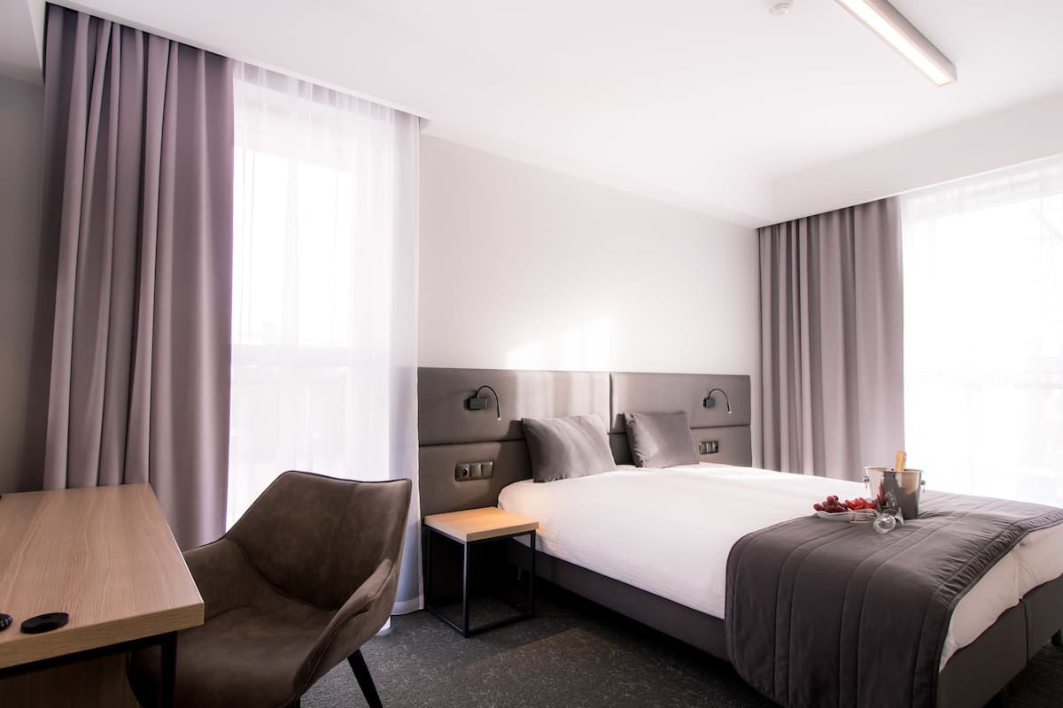 Una habitación de hotel con una cama, un escritorio, una silla y una mesita de noche.