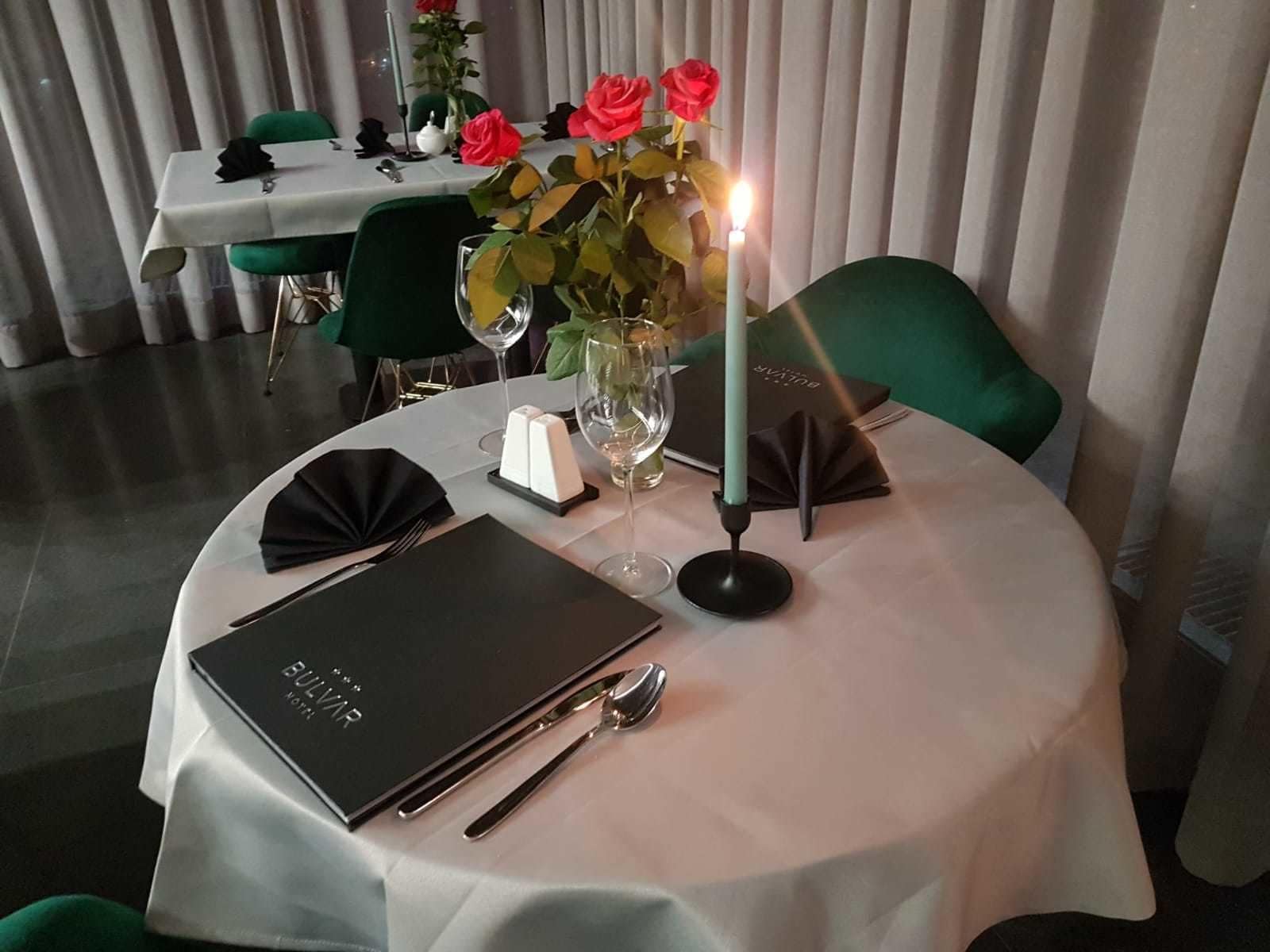 A dining table set with a menu, cutlery, a candle, and a vase of flowers.