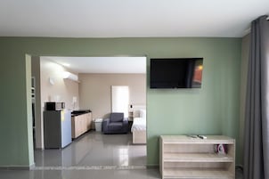 Habitación de hotel moderna con kitchenette, televisor de pantalla plana, zona de estar y vista al pasillo.