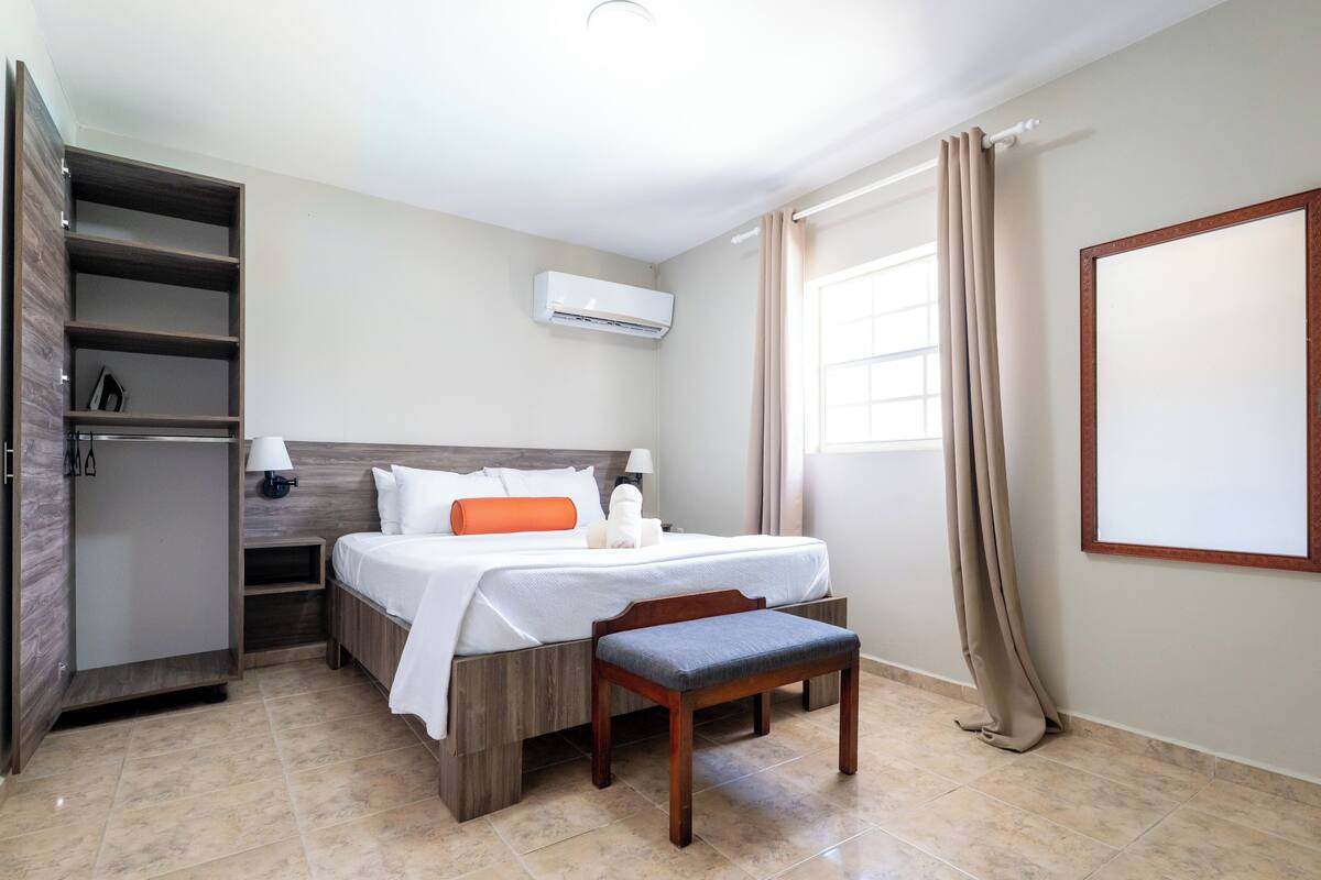Una camera d'albergo con un letto, una panca, un armadio e una finestra con tende.