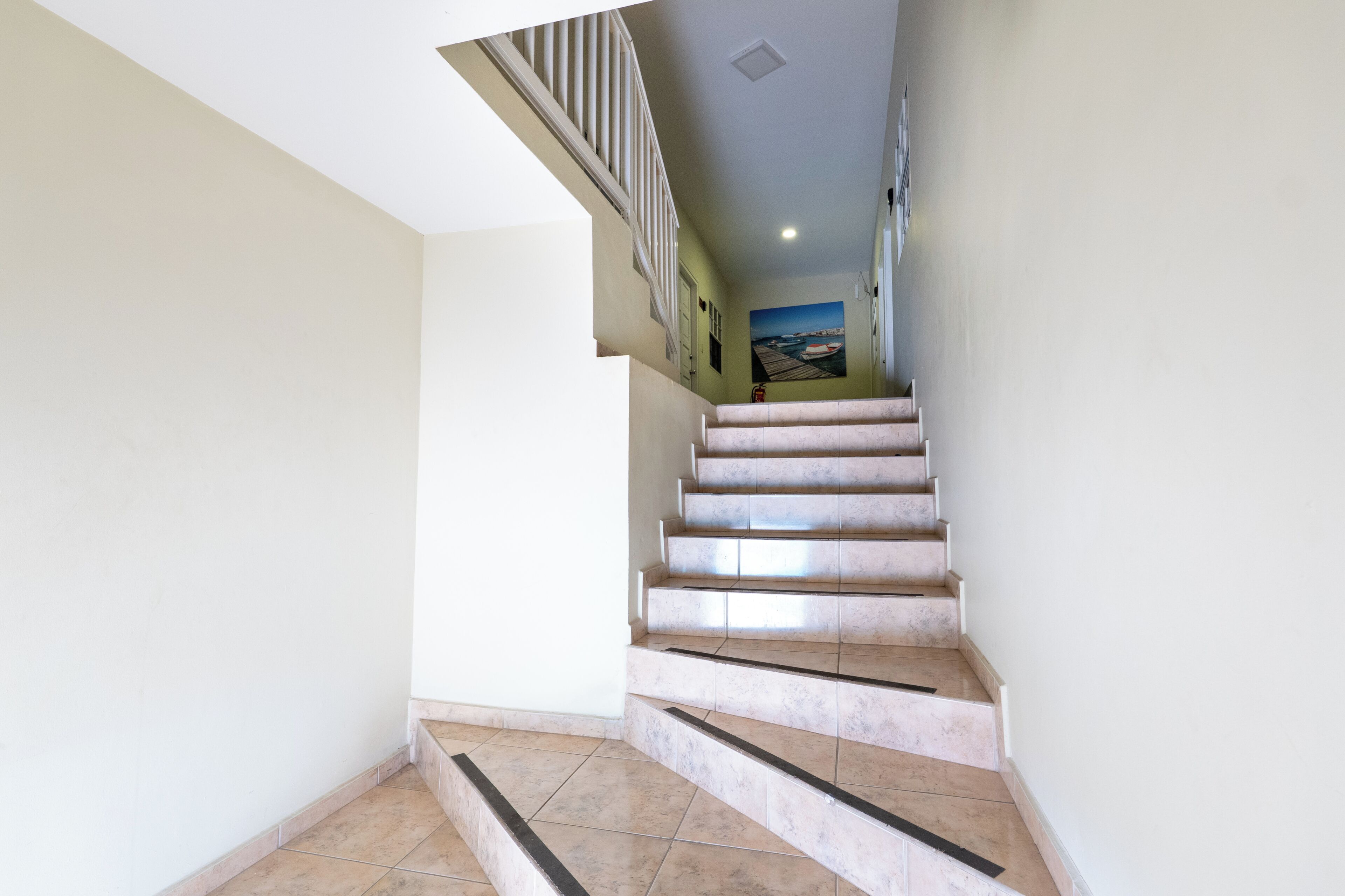 A staircase with a handrail, leading to a landing with a door and a wall-mounted picture.