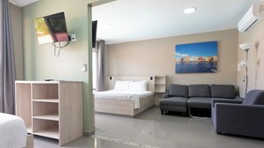 A hotel room with a bed, a sofa, a TV mounted on the wall, and a painting. - Delynne Boutique Hotel (Willemstad)