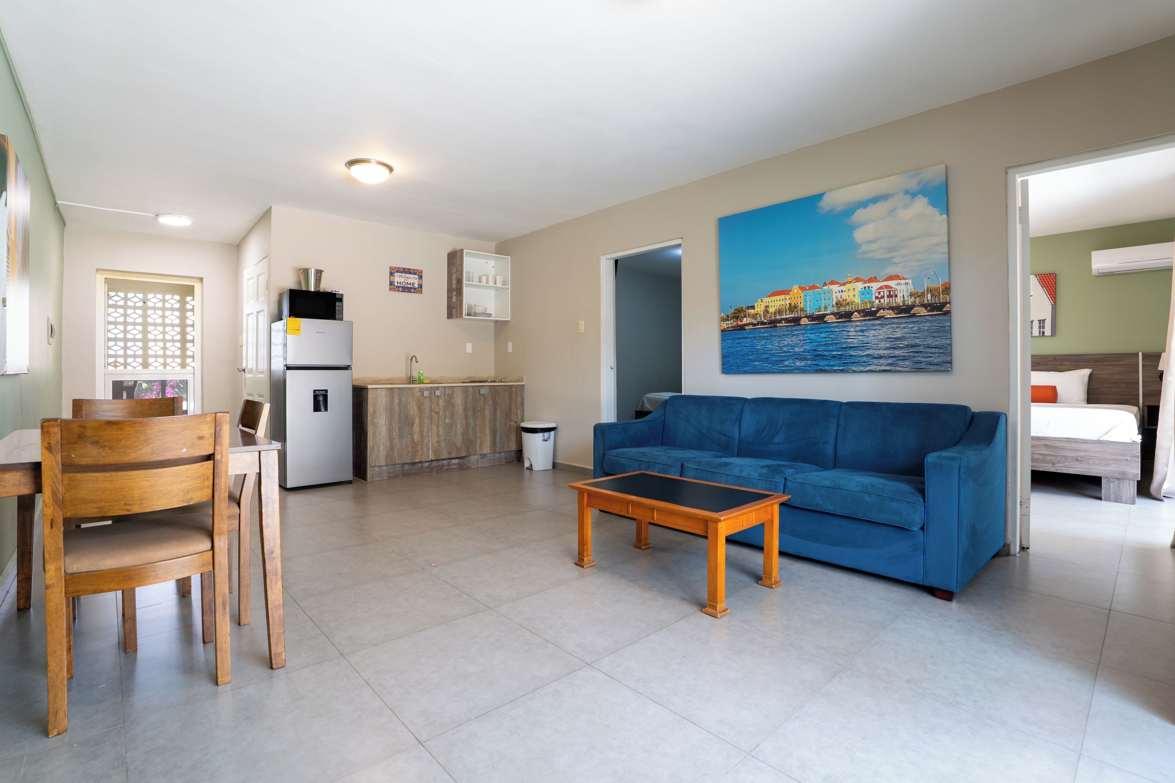 A living room with a blue sofa, wooden coffee table, and a painting of a waterfront scene.
