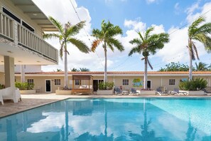 A pool area with lounge chairs, palm trees, and a building with a balcony. - Delynne Boutique Hotel (Willemstad)