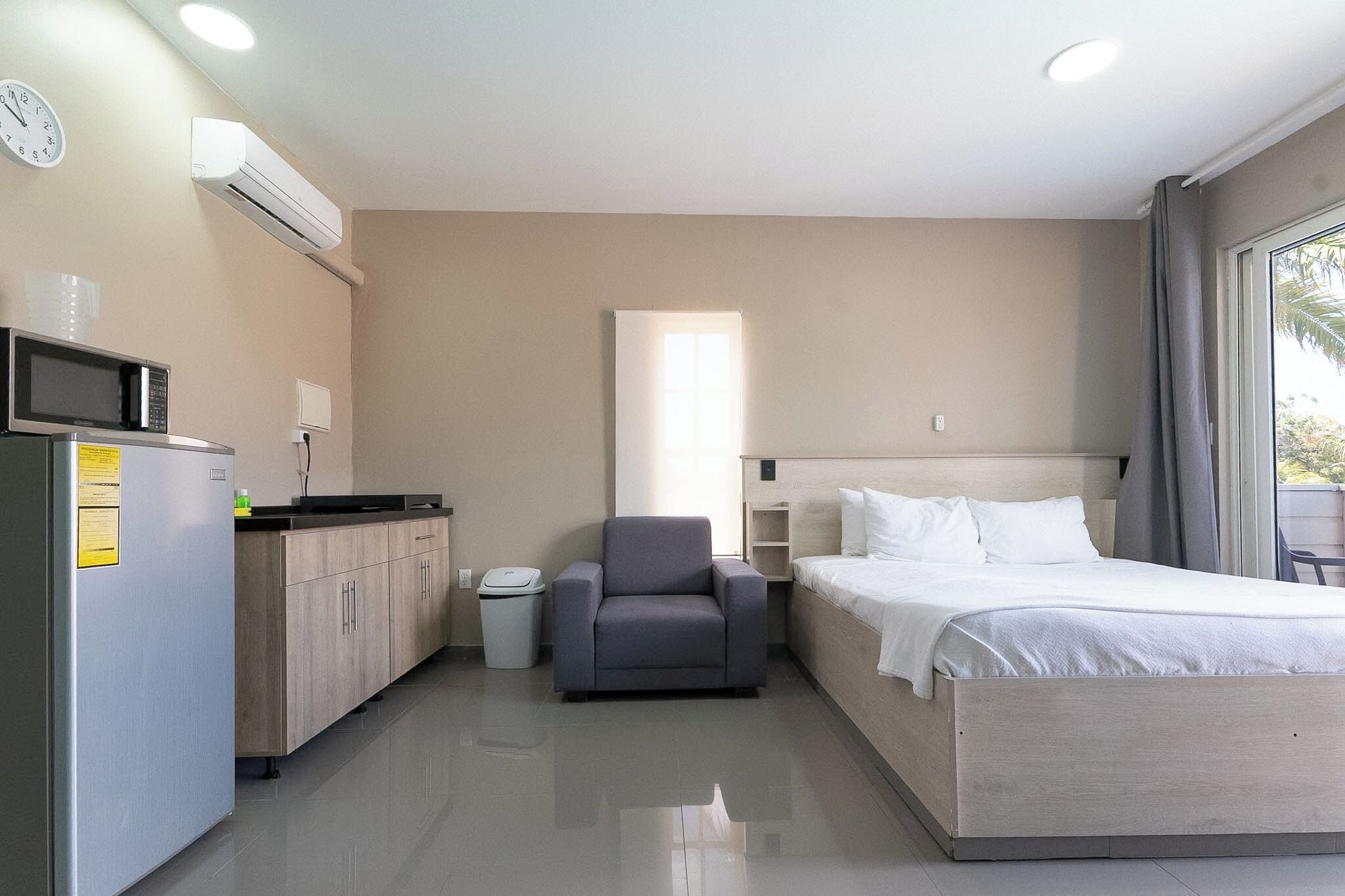 Una habitación de hotel con cama, una silla, microondas, cubo de basura y ventana con cortinas.