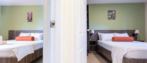 Two twin beds with white linens and orange pillows, a wooden headboard, and a green wall with a floral painting.