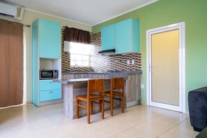 A kitchen with teal cabinets, a microwave, and a window with a brown valance. - Delynne Boutique Hotel (Willemstad)
