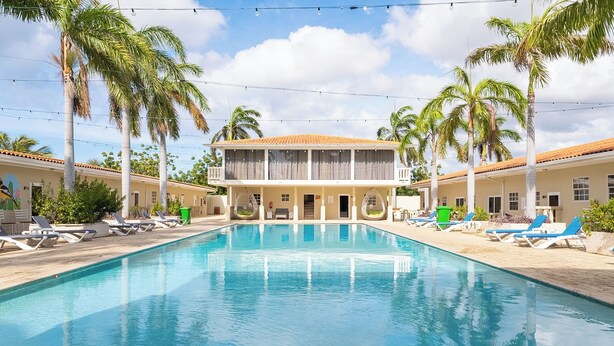 A swimming pool with lounge chairs, palm trees, and a building with a tiled roof. - Delynne Boutique Hotel (Willemstad)