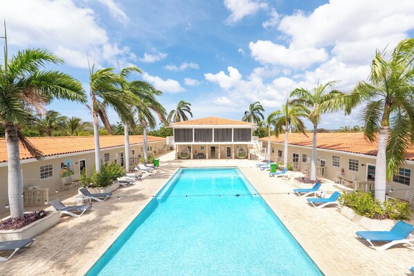 A pool area with lounge chairs, palm trees, and a building with a tiled roof.