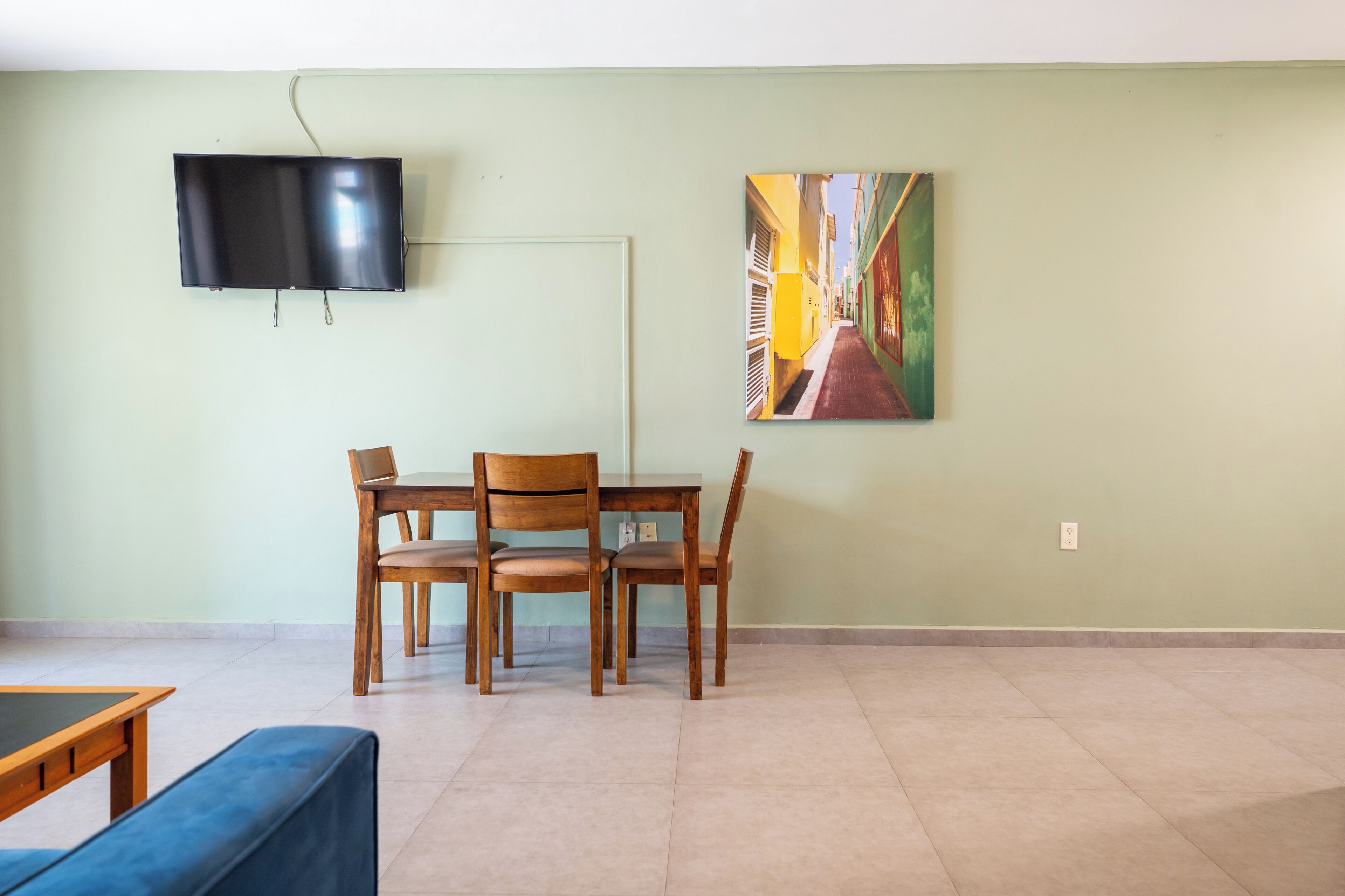 Uma área de jantar com uma mesa e cadeiras, uma TV de tela plana na parede e uma pintura de uma cena urbana.