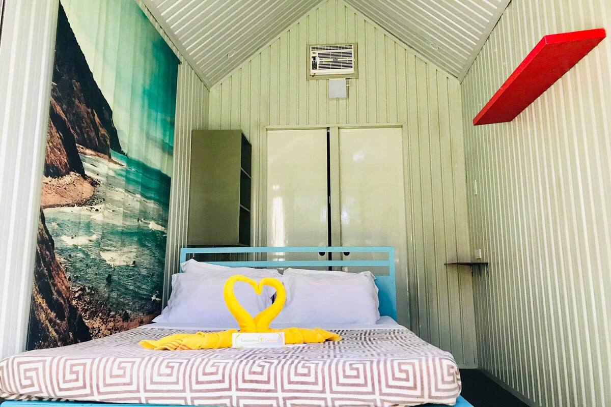 Una cama individual con una colcha estampada, una toalla decorativa con forma de corazón y un cuadro de una escena costera.