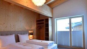 Quarto com uma cama grande, vigas de madeira no teto, luminária pendente e porta de correr de vidro para o exterior.