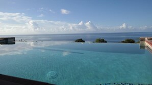 Una piscina infinita con agua cristalina azul, vista al océano y islas lejanas.