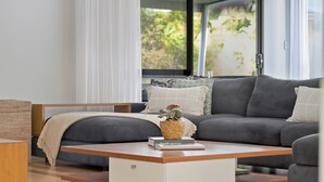 Un salon moderne avec un canapé gris, une table basse en bois et une grande fenêtre donnant sur un paysage verdoyant.