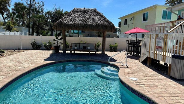 A swimming pool with a thatched roof structure, a poolside area with chairs, and a sign indicating pool rules. - The Lazy Tiki - Private Pool (Fort Myers Beach)