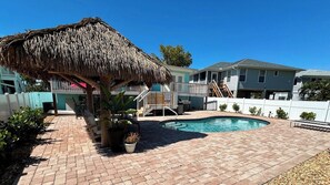 A backyard with a swimming pool, a thatched-roof structure, and a wooden deck.