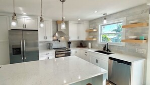 A modern kitchen with white cabinets, stainless steel appliances, and marble countertops. - The Lazy Tiki - Private Pool (Fort Myers Beach)
