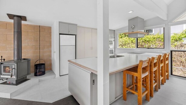 A modern kitchen with a built-in stove, white cabinetry, and a large window overlooking greenery. - Maddlyn with  Ocean Views & Peaceful Treed Retreat (Lorne)