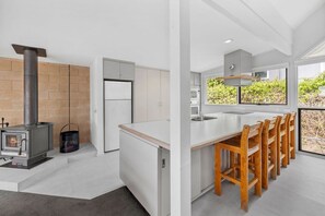 A modern kitchen with a built-in stove, white cabinetry, and a large window overlooking greenery.