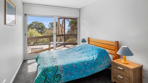 A bedroom with a bed, a nightstand, a lamp, and a sliding glass door leading to a balcony. - Maddlyn with  Ocean Views & Peaceful Treed Retreat (Lorne)