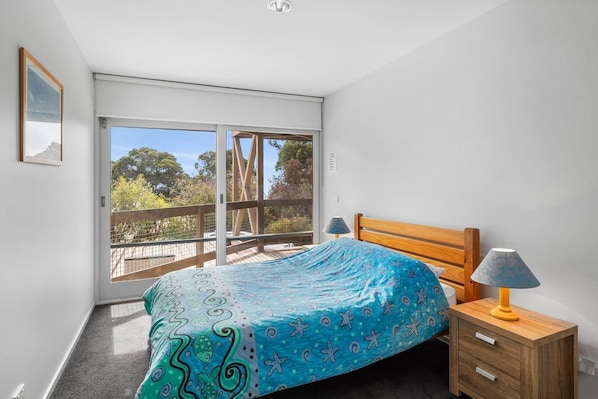 A bedroom with a bed, a nightstand, a lamp, and a sliding glass door leading to a balcony.