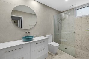 Uma casa de banho moderna com espelho redondo, lavatório azul, sanita e cabine de duche com vidro.