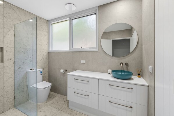 A modern bathroom with a glass shower enclosure, a toilet, a vanity with a sink, and a mirror. - Maddlyn with Ocean Views & Peaceful Treed Retreat (Lorne)