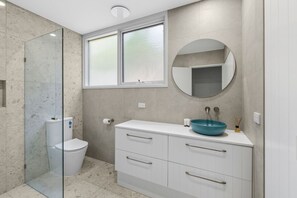 A modern bathroom with a glass shower enclosure, a toilet, a vanity with a sink, and a mirror. - Maddlyn with Ocean Views & Peaceful Treed Retreat (Lorne)