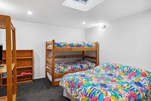 Uma cama de beliche com roupa de cama colorida, uma estante de madeira e um claraboia.