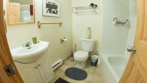 A bathroom with a sink, toilet, and bathtub. There is a towel rack above the toilet and a mirror on the wall. - Rent a Room at Cabot Shores - We are on the Cabot Trail (Englishtown)