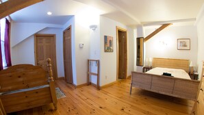 A bedroom with a wooden floor, a bed with a wicker headboard, a wooden wardrobe, and a door leading to another room. - Rent a Room at Cabot Shores - We are on the Cabot Trail (Englishtown)