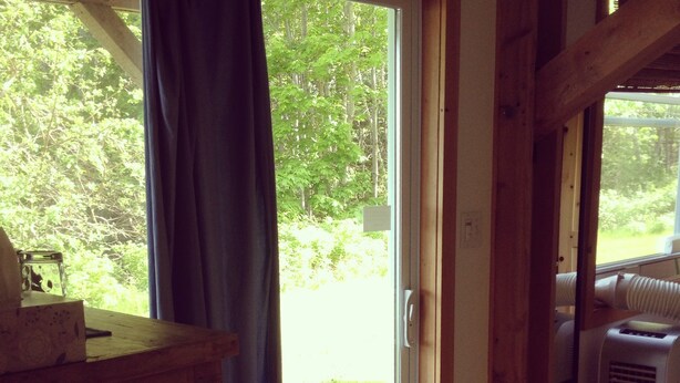 A room with a wooden floor, a sliding glass door leading to a grassy area, and a radiator on the right. - Rent a Room at Cabot Shores - We are on the Cabot Trail (Englishtown)