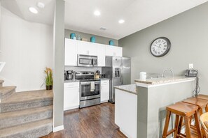 A modern kitchen with white cabinets, stainless steel appliances, a granite countertop, and a clock on the wall. - Your VIP Home in Orlando - Disney! (Kissimmee)