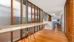 A modern interior with a long wooden desk, two chairs, and a view of the ocean through large windows. - Seaview Tce - Spectacular Home with Stunning Ocean and Headland Views (SUNSHINE BEACH)