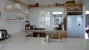 Une cuisine avec des plans de travail blancs, des étagères en bois et un réfrigérateur.