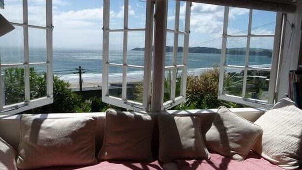 Une chambre dotée d’une grande baie vitrée donnant sur l’océan, d’un lit avec une literie rose et d’une vue sur la côte.