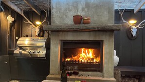 Une cuisine extérieure équipée d’un barbecue, d’une cheminée et d’une table où l’on sert du fromage, du vin et des fruits.