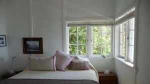 Une chambre avec un grand lit, une fenêtre donnant sur un paysage verdoyant, une table de chevet avec une lampe et un tableau encadré au mur.