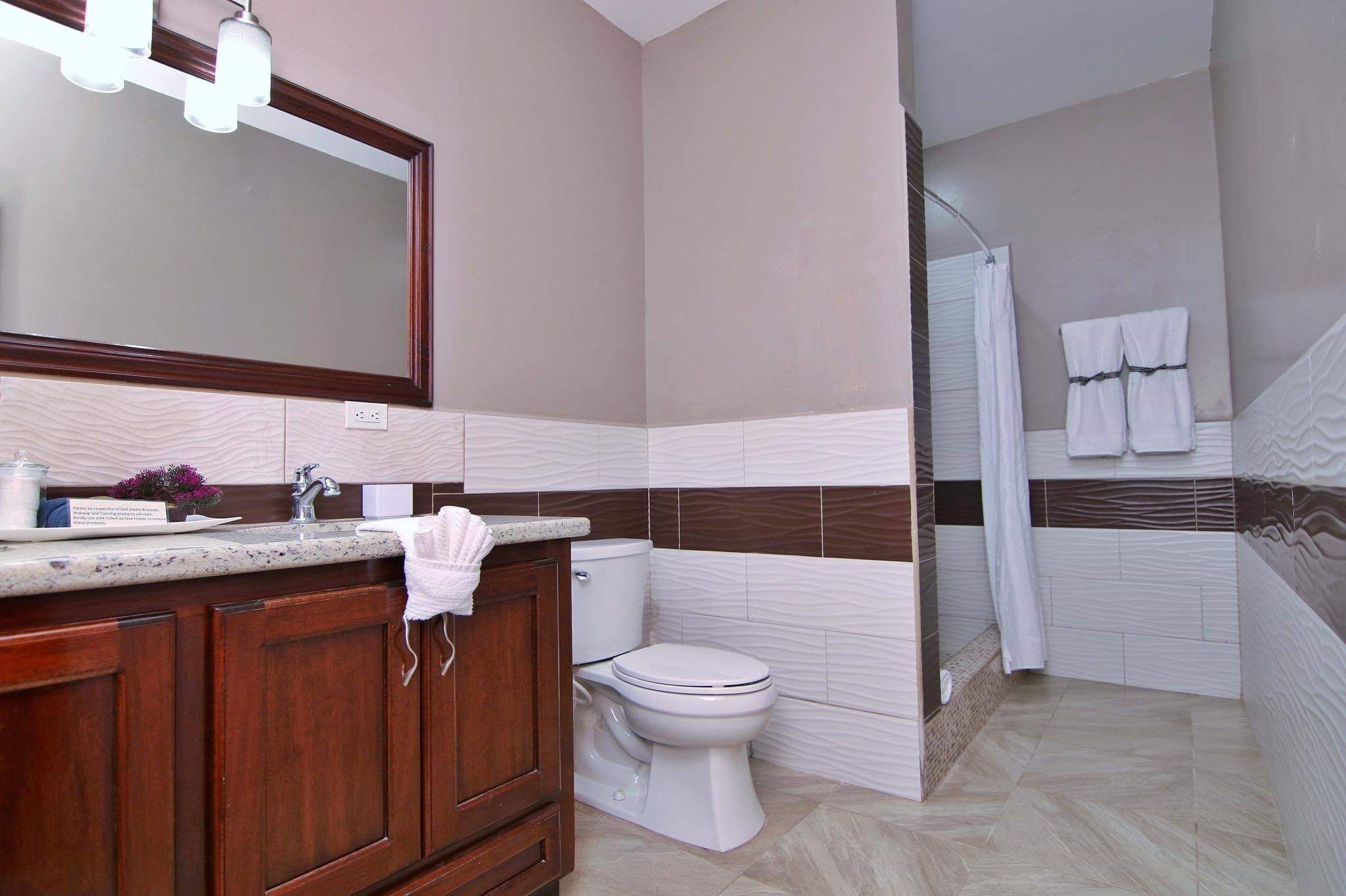 A modern bathroom with a large mirror, a sink with a towel, a toilet, and a shower area.