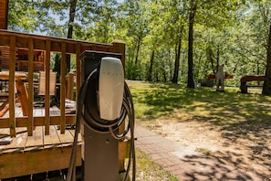 A Tesla charging station in a wooded area with a wooden deck and picnic table. - Real Log Cabin Near Big Cedar w Private Hot Tub & Grill on Huge Deck_Car Charger (Ridgedale)