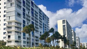 A modern high-rise building with multiple balconies, located near a sandy beach with sparse vegetation. - Stay Near Deerfield Beach Pier, Enjoy Our Cozy 1-bedroom Apartment (Deerfield Beach)