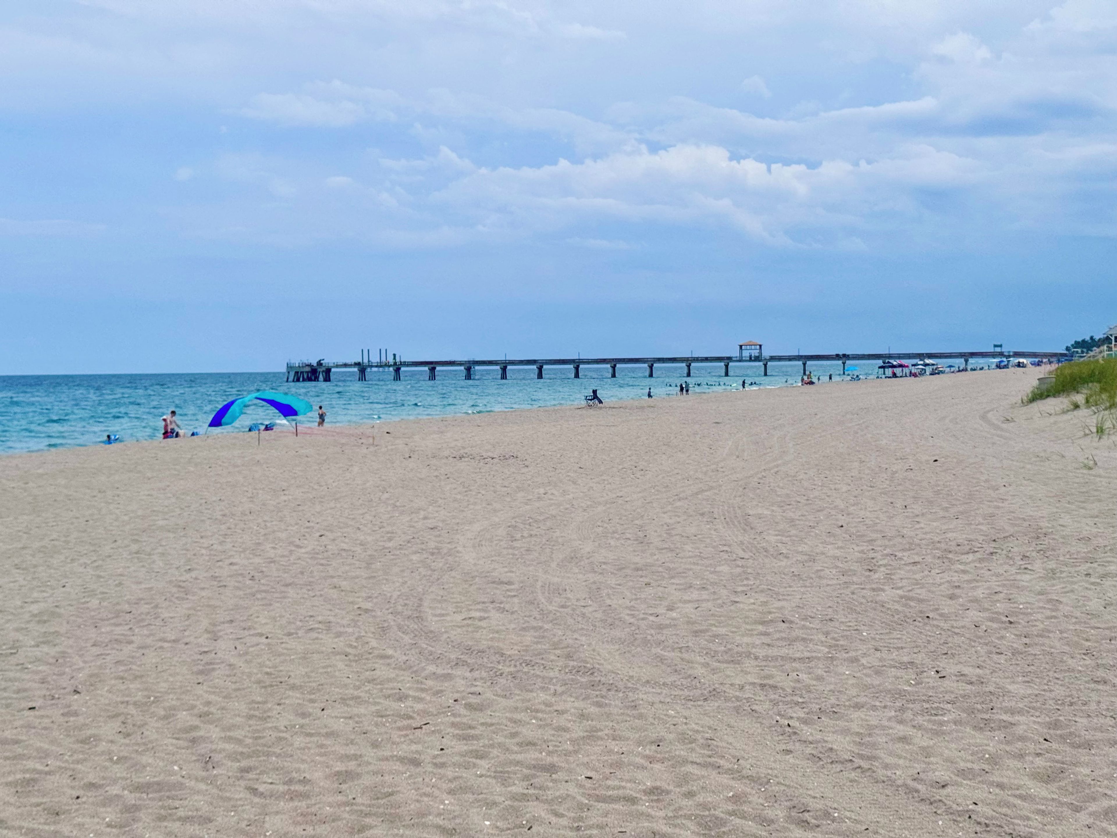 A beach with a pier extending into the water, sandy terrain, and a clear sky.