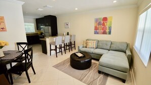 A modern living room with a sofa, ottoman, and dining area with chairs and a table. - Stay Near Deerfield Beach Pier, Enjoy Our Cozy 1-bedroom Apartment (Deerfield Beach)