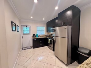A modern kitchen with dark cabinets, a stainless steel refrigerator, and a tiled floor. - Stay Near Deerfield Beach Pier, Enjoy Our Cozy 1-bedroom Apartment (Deerfield Beach)
