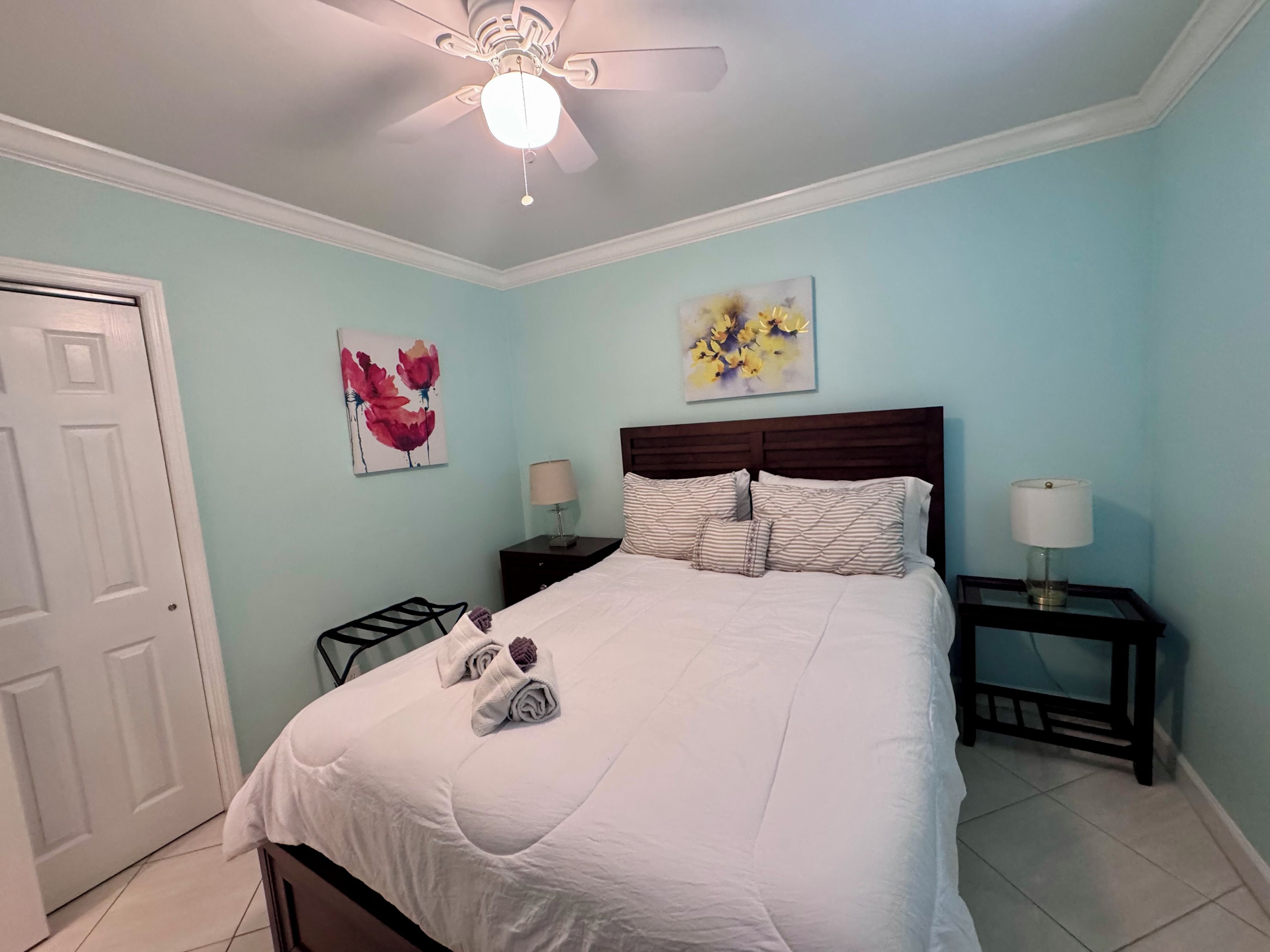 A bedroom with a bed, two bedside tables, a ceiling fan, and artwork on the walls.