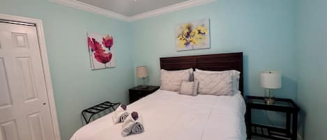 A bedroom with a bed, two bedside tables, a ceiling fan, and artwork on the walls.