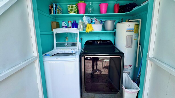 Een kleine wasruimte met een wasmachine, droger en planken met diverse spullen.